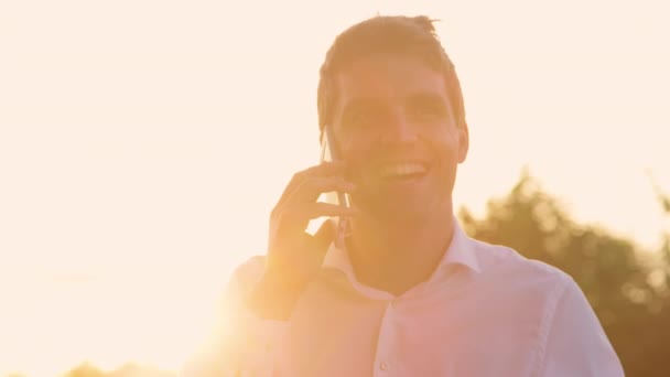 CLOSE UP: Successful businessman talks on the phone at golden summer sunset. — Stock Video