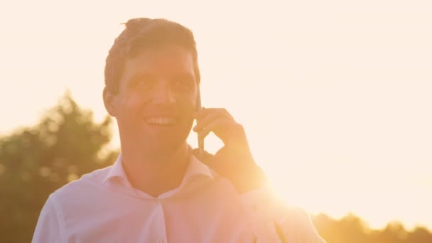 CLOSE UP: Man cheerfully talks on the phone on sunny evening after good meeting. — Stock Video