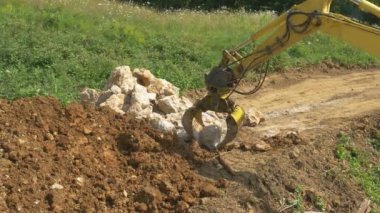 Kazı operatörü büyük kayaları bir kazıktan drenaj çukuruna aktarıyor..