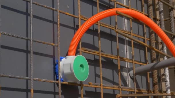 CLOSE UP: Thin corrugated orange conduit runs out of an electricity outlet. — Stock Video