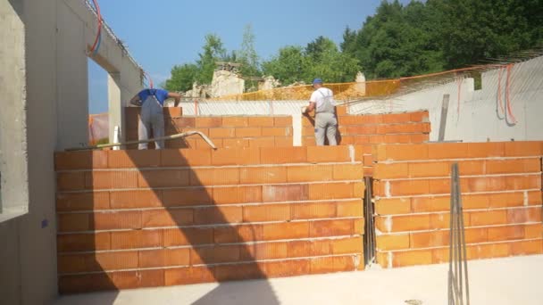 Dos contratistas ponen ladrillos dentro de una casa en construcción en un día soleado. — Vídeos de Stock
