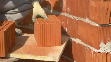 Tanınmayan erkek tuğla ustası, bir tuğlayı ikiye bölmek için balta kullanıyor..