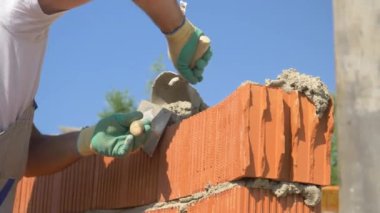 Güneşli bir günde tuğla döşeyen inşaatçının ellerinin detaylı görüntüsü..