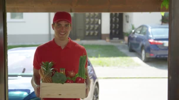 FERMER : Un coursier souriant portant une chemise rouge livre de l'épicerie à une jeune femme — Video