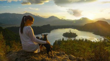 Gölün yukarısındaki bir kayanın üzerinde oturan dişi turist kanadı ve köpeğini okşadı..
