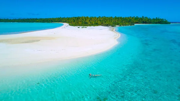 AERIALE: Giovane donna che si rilassa nell'acqua cristallina dell'oceano vicino alla lussureggiante isola esotica — Foto Stock