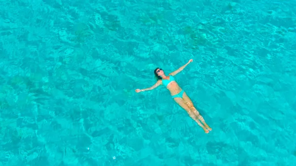 AERIAL: Volando por encima de chica turística relajada flotando en el agua cristalina del océano. — Foto de Stock