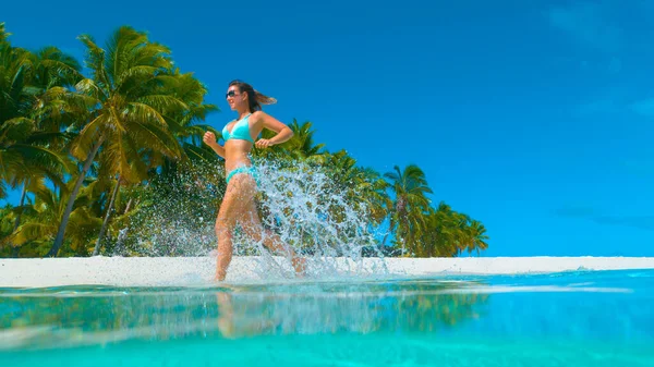 ÁNGULO BAJO: Mujer despreocupada corriendo y salpicando el agua cristalina del océano. —  Fotos de Stock
