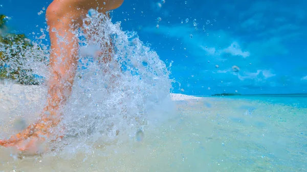 CHIUDI: Donna irriconoscibile spruzza acqua mentre corre lungo la spiaggia tropicale. — Foto Stock