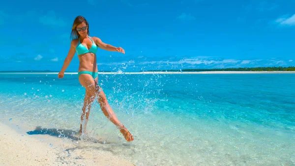 LOW Kąt: radosna dziewczyna w bikini kopiąca i pluskająca szklaną wodą oceanu. — Zdjęcie stockowe