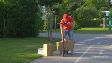 Postacı paketleri teslim ederken elektrikli scooterının üstüne üç kutu dizer..