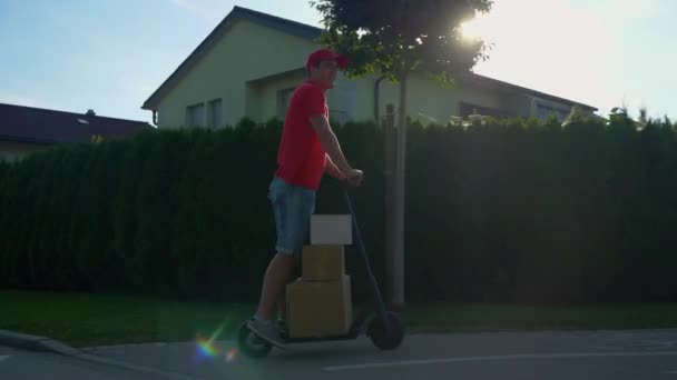 LENS FLARE: Dostawca bawiący się transportem paczek na skuterze elektrycznym. — Wideo stockowe