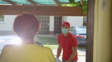 Genç kurye kapı ziline cevap veren yaşlı kadına bir paket atıyor.