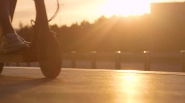 Düşük açılı, tanınmayan bir adam güneşli bir yaz akşamında elektrikli scooter kullanıyor.