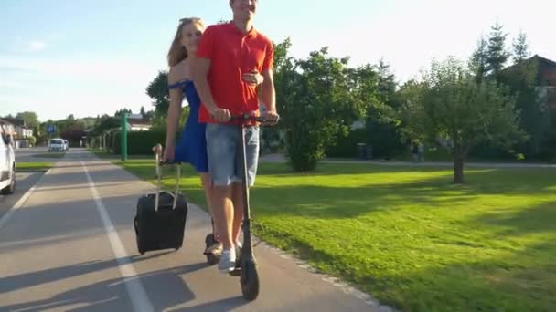 FECHAR UP: Homem e mulher montam uma scooter elétrica juntos no caminho para o aeroporto — Vídeo de Stock