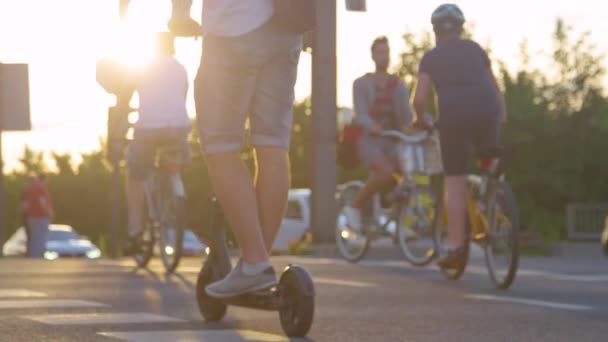 LOW ANGLE: Man paardrijden een e-scooter en fietsers steken de weg bij zonsopgang. — Stockvideo