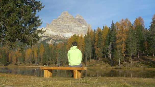 コピースペース:男はベンチに座って、秋の山と湖の風景を観察する — ストック動画