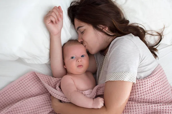Όμορφη μελαχρινή κορίτσι που φιλάει το μωρό της. Είναι στην κρεβατοκάμαρα. — Φωτογραφία Αρχείου