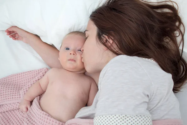 Beautiful brunette girl kissing her baby. They're in the bedroom — Stock Photo, Image