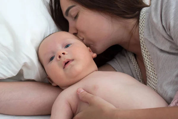 Beautiful brunette girl kissing her baby. They're in the bedroom — Stock Photo, Image