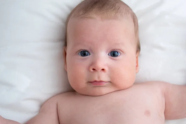 Bambino felice sdraiato su una coperta bianca. Il concetto di purezza e — Foto Stock