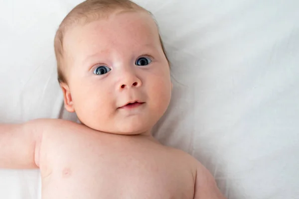 Bambino felice sdraiato su una coperta bianca. Il concetto di purezza e — Foto Stock