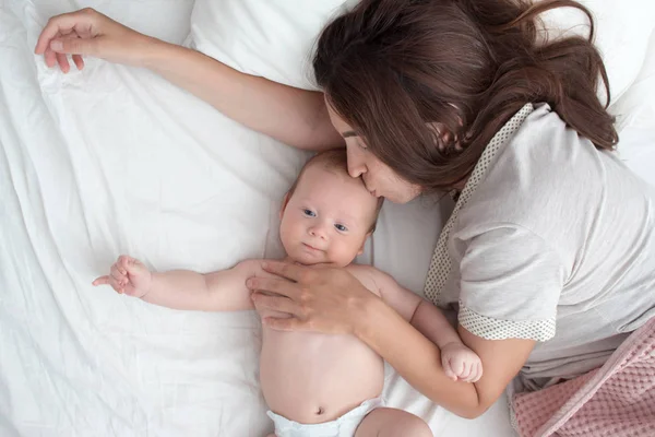 Beautiful brunette girl kissing her baby. They're in the bedroom — Stock Photo, Image