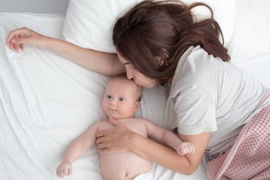 Güzel esmer kız bebeğini öpüyor. Yatak odasındalar.