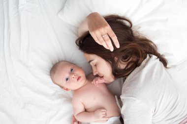 Güzel esmer kız bebeğini öpüyor. Yatak odasındalar.