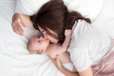 Güzel esmer kız bebeğini öpüyor. Yatak odasındalar.