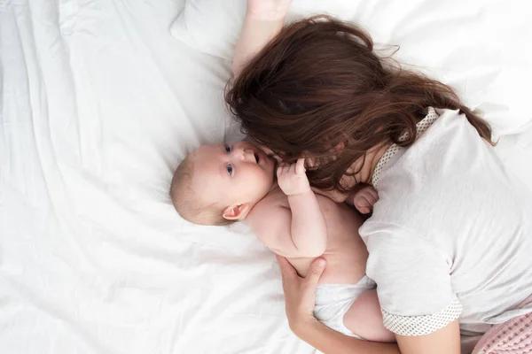 Όμορφη μελαχρινή κορίτσι που φιλάει το μωρό της. Είναι στην κρεβατοκάμαρα. — Φωτογραφία Αρχείου