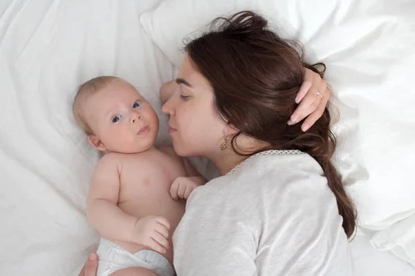 Beautiful brunette girl kissing her baby. They're in the bedroom — Stock Photo, Image