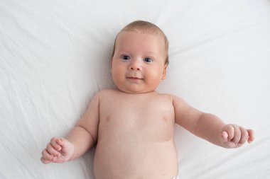 Beyaz bir battaniyenin üzerinde yatan mutlu bebek. Saflık ve j kavramı