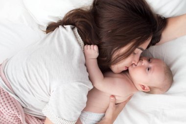 Güzel esmer kız bebeğini öpüyor. Yatak odasındalar.