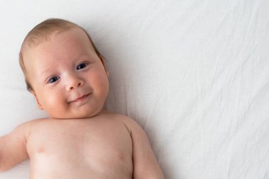 Beyaz bir battaniyenin üzerinde yatan mutlu bebek. Saflık ve j kavramı