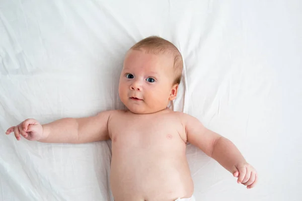 Bambino felice sdraiato su una coperta bianca. Il concetto di purezza e — Foto Stock
