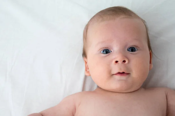 The surprised baby lies on a white blanket. The concept of inter — Stock Photo, Image