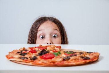 Küçük kız pizzaya bakıyor. Çocuk pizza buldu