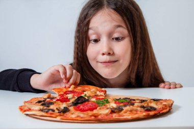 Küçük kız bir dilim pizza alıyor. Çocuk pizza yiyor.