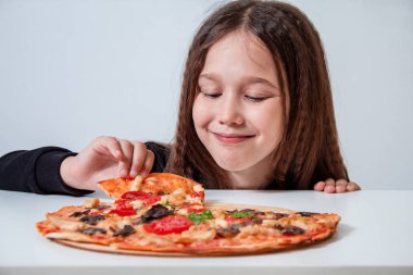 Küçük kız bir dilim pizza alıyor. Çocuk pizza yiyor.