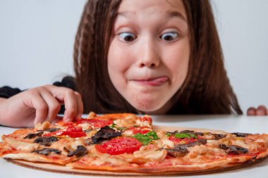 Küçük kız bir dilim pizza alıyor. Çocuk pizza yiyor.