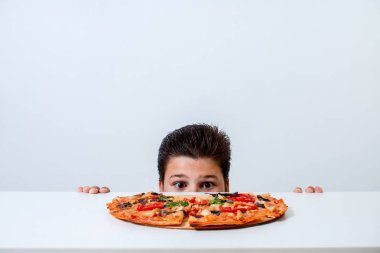 Çocuk İtalyan pizzası yiyor. Masanın arkasından bakar