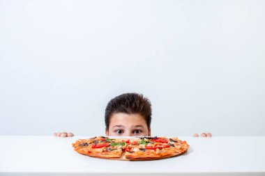 Çocuk İtalyan pizzası yiyor. Masanın arkasından bakar