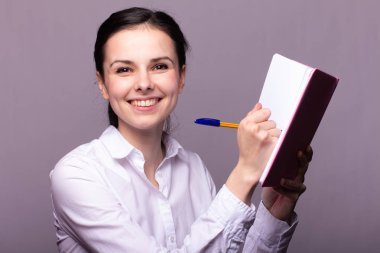 beyaz gömlekli kız elinde pembe bir defter tutar