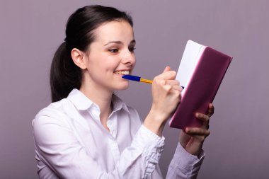 beyaz gömlekli kız elinde pembe bir defter tutar