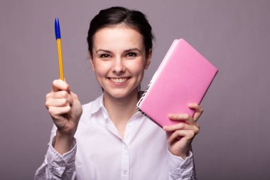 beyaz gömlekli kız elinde pembe bir defter tutar