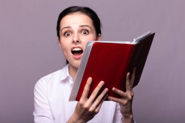 beyaz gömlekli kız elinde kırmızı bir defter tutar