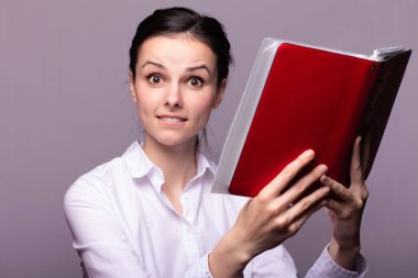 beyaz gömlekli kız elinde kırmızı bir defter tutar