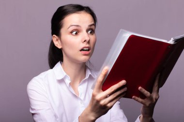 beyaz gömlekli kız elinde kırmızı bir defter tutar