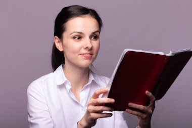 beyaz gömlekli kız elinde kırmızı bir defter tutar
